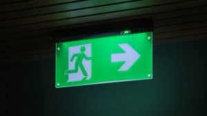 A green exit sign glowing in the darkness, indicating a way out with a rightward arrow.