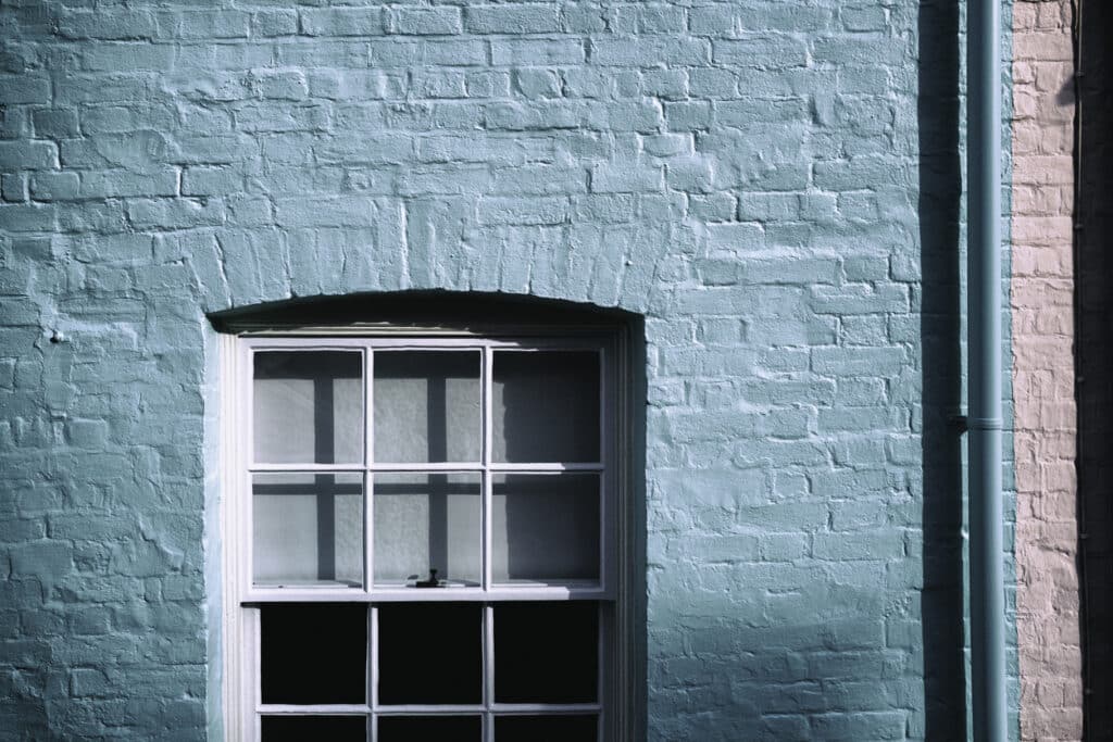 Abstract view of a newly painted English brick built cottage and its contemporary sash window seen in harsh evening light. A pink pained terraced house can just be seen on the right.